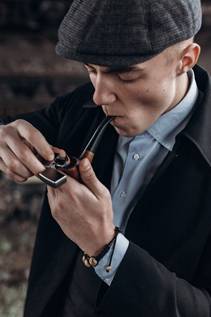 sherlock holmes look, man in retro outfit, smoking, lighting wooden pipe. england in 1920s theme. fashionable confident gangster. atmospheric moments. space for textの写真素材