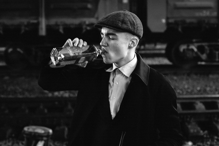 stylish gangster man drinking. posing on background of railway. england in 1920s theme. fashionable brutal confident guy. atmospheric  moments. space for text.black white photoの写真素材
