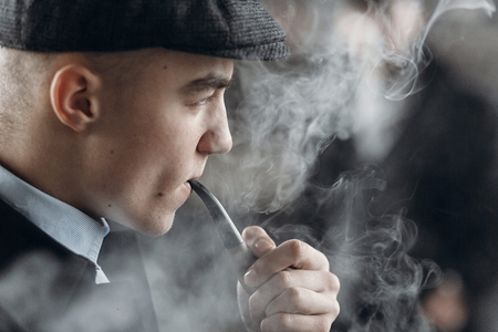 stylish man in retro outfit, smoking wooden pipe. sherlock holmes look cosplay.  england in 1920s theme. fashionable confident gangster. atmospheric momentsの写真素材