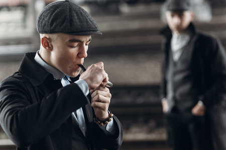 stylish gangsters men, smoking pipe on background of railway. england in 1920s theme. fashionable brutal confident man. atmospheric smoky moments. space for textの写真素材