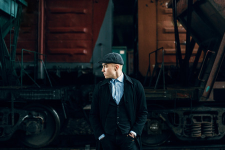 stylish gangster in tweed outfit posing on background of railway carriage. england in 1920s theme....