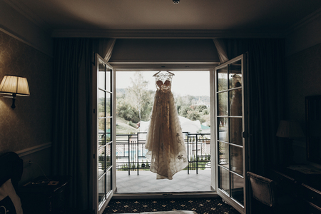 luxury wedding dress hanging on window in a hotel room. silhouette of amazing bride's gown in light. morning preparation, getting ready. space for text . wedding morningの写真素材