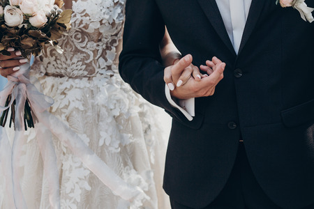 luxury wedding couple hugging and holding golden bouquet of roses with ribbons  in park. stylish...