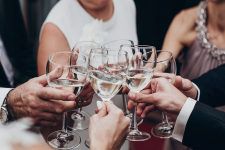 people toasting with champagne and wine glasses in hands clinking at luxury wedding reception at restaurant. cheering at stylish celebration. luxury life concept. space for text.の写真素材