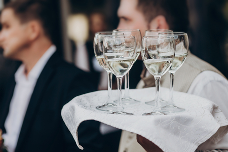 champagne and wine glasses on tray at luxury wedding reception at restaurant.  waiter serving drinks among guests at stylish celebration. luxury life concept. space for textの写真素材