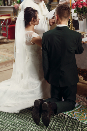 gorgeous wedding couple standing at altar making vows at official ceremony in old church. traditional moment of marriage of bride and stylish groomの写真素材