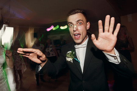 happy stylish groom dancing and having fun at wedding party in restaurant reception. funny excited moment of emotional bride and dance. space for textの写真素材