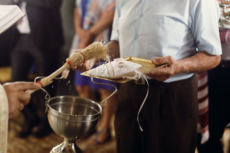 Orthodox christian priest showering golden wedding rings on white pillow with holy water, sacred...