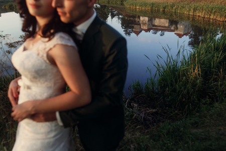 reflection of castle in lake and stylish luxury bride and groom hugging tender and posing in soft light at sunset.  unusual moment of beautiful wedding couple outdoorsの写真素材