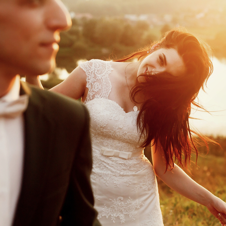 gorgeous bride and stylish groom smiling and having fun in the evening warm sunlight. sensual romantic moment of luxury wedding couple in amazing sunsetの写真素材