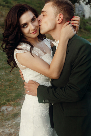 stylish luxury bride and groom kissing gently together near old castle wall at sunset. sensual moment of beautiful wedding couple outdoorsの写真素材