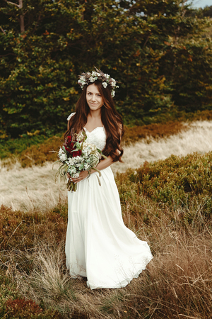 stylish bride posing with bouquet on background of forest, luxury boho wedding at mountainsの写真素材