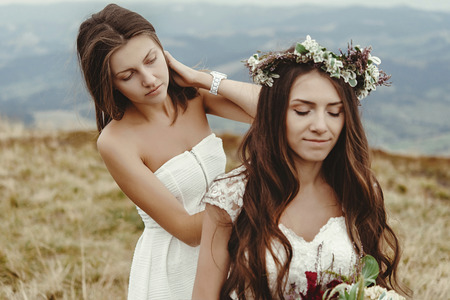 stylish bridesmaid helping gorgeous bride preparing, boho wedding, luxury ceremony at mountainsの写真素材
