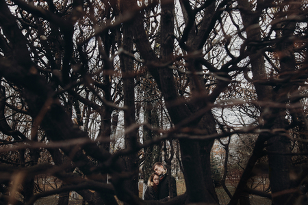 stylish hipster man and woman under branches hugging gently, tender touch in autumn park. sensual atmospheric moment with space for text. creative photoの写真素材