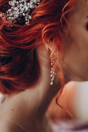 stylish bride detail, luxury earring jewelry and red hair curl, beautiful wedding dress. rustic wedding morning preparation. bridal getting ready. emotional moment. space for textの写真素材
