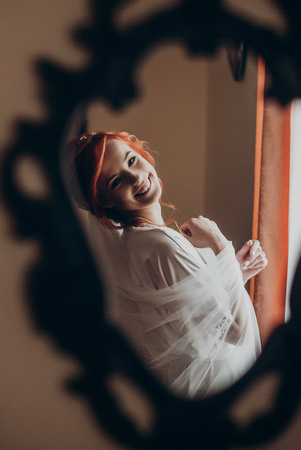 happy stylish bride in silk robe looking in mirror on the wall and smiling.  rustic wedding morning preparation. portrait reflection of young woman. space for text. luxury brideの写真素材