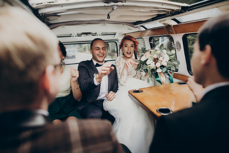 stylish happy bride and groom having fun and dancing inside of retro car smiling. emotional moment, space for text. luxury wedding newlyweds party with bridesmaids and groomsmenの写真素材