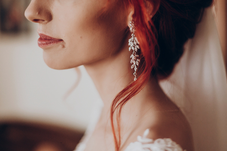 stylish bride detail, luxury earring and red hair curl, beautiful wedding dress. rustic wedding morning preparation. bridal getting ready. emotional moment. space for textの写真素材