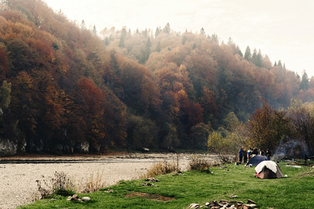group of friends camping at the riverside with tent and fire at beautiful woods in  mountains, national parkの写真素材