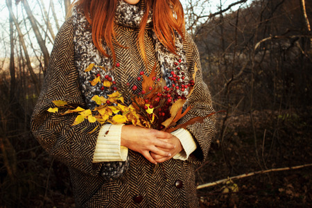 beautiful stylish happy gorgeous girl holding amazing bouquet of leaves and berries on the background of sunny autumn forestの写真素材