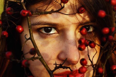 gorgeous stylish beautiful happy brunette girl and red berries of hawthorn on a background of sunny autumn forestの写真素材