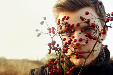 gorgeous stylish beautiful handsome blonde boy and red berries of hawthorn on a background of sunny autumn forestの写真素材