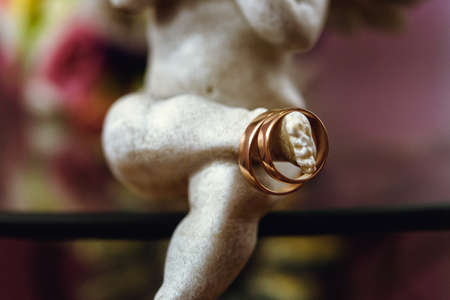 golden wedding rings on beautiful angel on the background of bride bouquetの写真素材