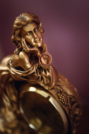 stylish pair of golden wedding ring on metal gold woman figurine with clock, time conceptの写真素材