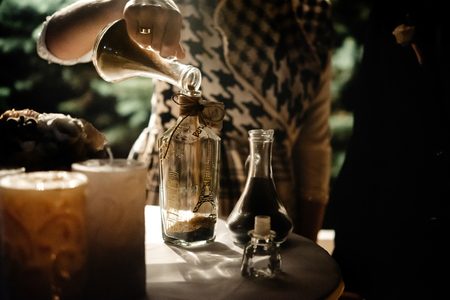 bride and groom holding and pouring  glass jars with sand for wedding tradition ritual at evening receptionの写真素材