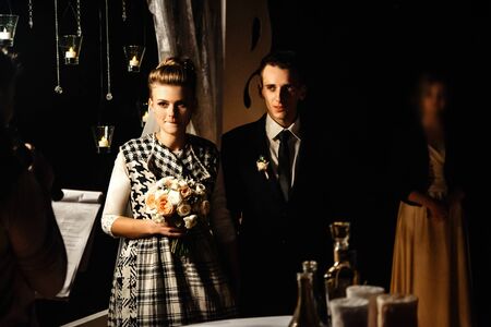 gorgeous bride and stylish groom at evening wedding ceremony walking down with candles, luxury ...