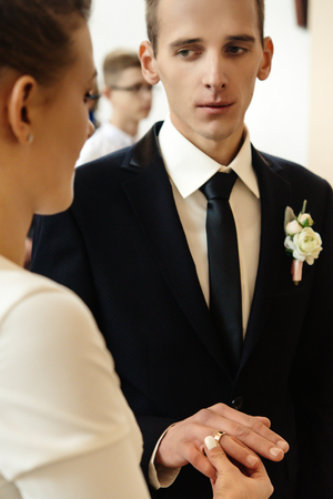 happy stylish bride and elegant groom exchanging wedding rings at ceremony at churchの写真素材