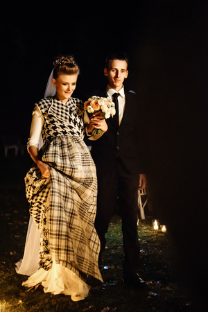 gorgeous bride and stylish groom at evening wedding ceremony walking down with candles, luxury  reception in restaurantの写真素材