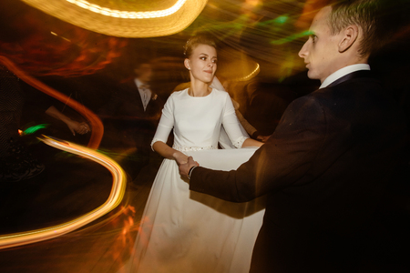 gorgeous bride and stylish groom emotionally dancing, luxury wedding reception in restaurant, cool motion lightの写真素材
