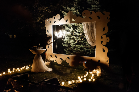 candle light in glass lanterns and wooden arch and lamp at luxury wedding ceremony in evening, decor and arrangementsの写真素材
