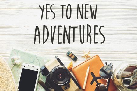 new adventure text sign concept. say yes to new adventures. time to travel, wanderlust background flat lay. camera sunglasses passport money map phone hat car plane  on white wooden table top viewの写真素材