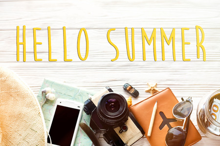 hello summer text, travel wanderlust concept, space for text, flat lay. map camera sunglasses passport money phone hat shells car  on white wooden background top view. planning holidayの写真素材