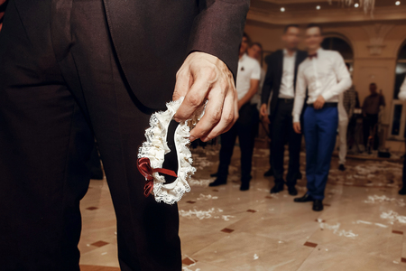 groom holding silk garter from bride at wedding party. tradition of throwing bridal garter to man, having fun at  wedding reception in restaurant.の写真素材