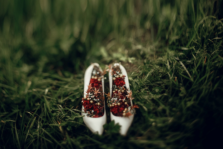 beautiful white shoes with red bouquets on green grass close up in the morning. space for text. bride getting ready for weddingの写真素材