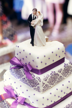 bride and groom on wedding cake. figurines on cake top with purple icing, luxury wedding reception, catering in restaurantの写真素材