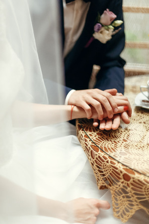 stylish wedding couple holding hands, sitting at wooden vintage table with warm coffee in cups in cafe. happy  bride and groom in dress and suit  huggingの写真素材