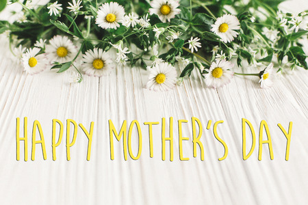 happy mother's day text sign. greeting card. gentle daisy flowers on white rustic wooden background. tender soft image. mothers day concept. fresh yellow herbsの写真素材