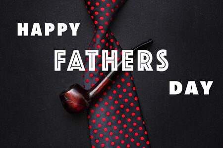 happy father's day text sign on tie and smoking pipe on black rustic background top view. fathers day greeting card concept. minimalistic flat lay. space for text. gentleman setの写真素材