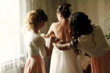 beautiful bridesmaids in pink dresses helping bride get dressed in gown in the morning, bridal morning, wedding preparationの写真素材