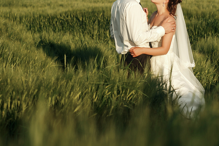 happy stylish bride and groom embracing in evening sun light in wheat meadow. gorgeous wedding couple hugging in sunlight in summer field. newlyweds in summerの写真素材