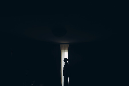 groom getting ready in the morning before wedding ceremony, putting on jacket on shirt in room silhouetteの写真素材
