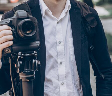 stylish man holding photo camera. professional holding video camera at wedding ceremony,...