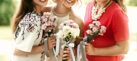 bride in vintage dress and bridesmaids with bouquets smiling and posing in sunny park at wedding receptionの写真素材