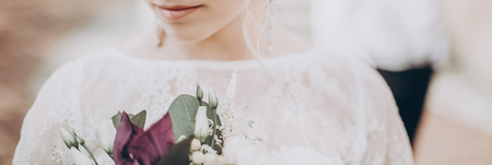 stylish wedding bride with bouquet. modern bride  holding fashionable bouquet, lips and earrings close up, on background of groom. fine art wedding photo, romantic moment, long edgeの写真素材