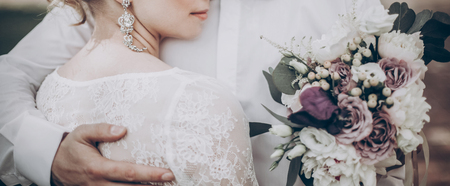 stylish wedding bride smiling, holding bouquet. modern bride hugging groom, lips and earrings close up. fine art wedding photo, romantic moment, long edgeの写真素材