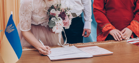 stylish wedding bride and groom signing wedding register. modern couple signs official document in office. romantic tender moment, official wedding ceremonyの写真素材